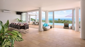 A spacious living area with a dining table set for a meal, a comfortable seating area with a view of the ocean, and a large window providing natural light. - Villa Monsoon 7-Bedroom with Breathtaking Panoramic Seaview (Amphoe Ko Samui)