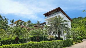 A modern two-story house with a balcony, surrounded by lush greenery and palm trees. - Villa Monsoon 7-Bedroom with Breathtaking Panoramic Seaview (Amphoe Ko Samui)