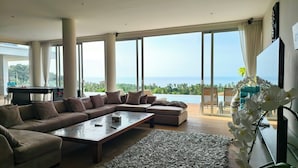 A spacious living room with a large sectional sofa, a coffee table, and a view of the ocean through floor-to-ceiling windows. - Villa Monsoon 7-Bedroom with Breathtaking Panoramic Seaview (Amphoe Ko Samui)