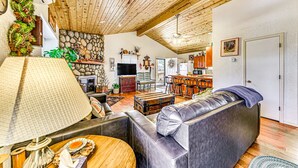 A cozy living room with a stone fireplace, leather sofa, and a wooden ceiling. - Wood Cabin, Full Amenities, Family Friendly and wifi access (Ruidoso)