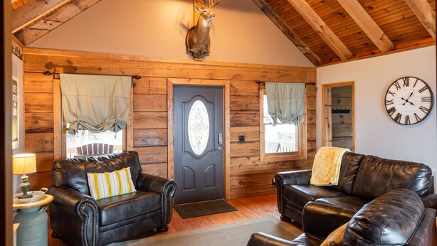 A log cabin interior with two leather sofas, a wooden ceiling, and a mounted deer head.