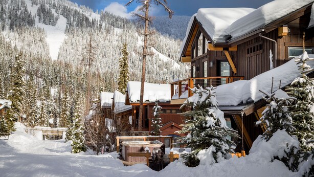 Eine Holzlodge mit Balkon, umgeben von schneebedeckten Bäumen und einem Berg im Hintergrund.