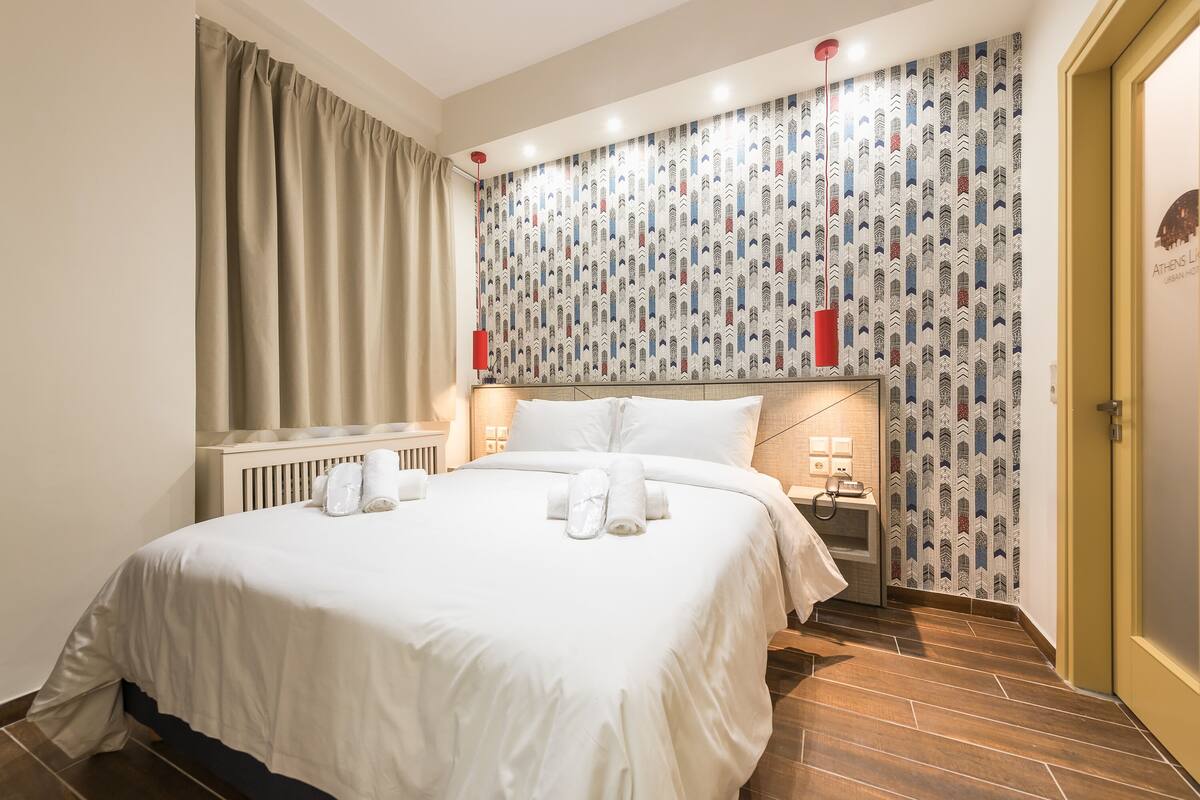 A hotel room with a large bed, a radiator, a patterned wallpaper, and a door with a sign.