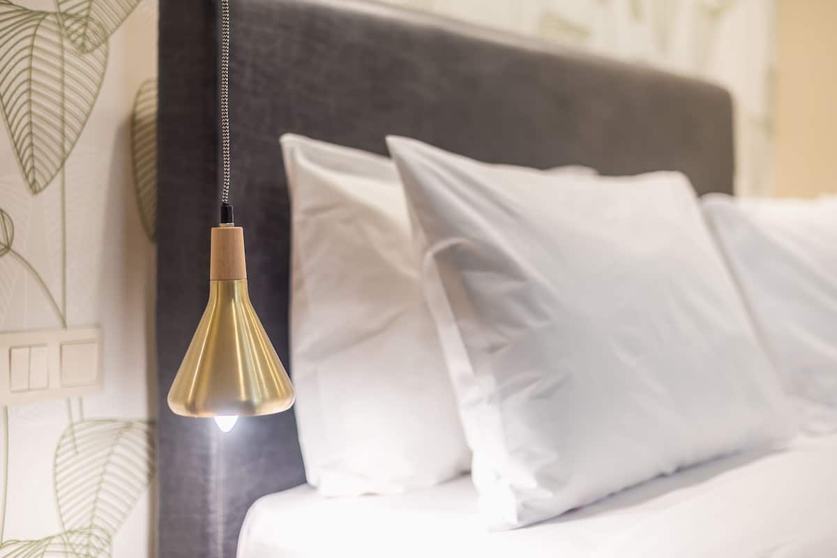 A bed with white pillows and a hanging pendant light.