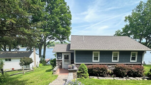 A two-story house with a stone pathway leading to the front door, surrounded by a well-maintained lawn and flowering plants. - WOLCOTT NY  Waterfront cottage rental on Port Bay seasonal available 2026 (Port Bay - Wolcott)