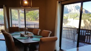 Ein Essbereich mit Tisch und Stühlen, einer Pendelleuchte und Blick auf eine Terrasse und Berge durch große Fenster.