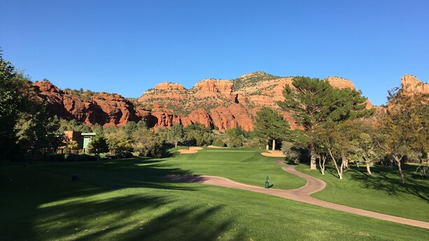 Ein Golfplatz mit blauem Himmel, grünem Gras und roten Felsformationen im Hintergrund.