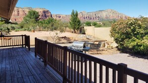 Eine Holzterrasse mit Grill und Sitzgelegenheit, mit Blick auf eine Wüstenlandschaft und rote Felsformationen.