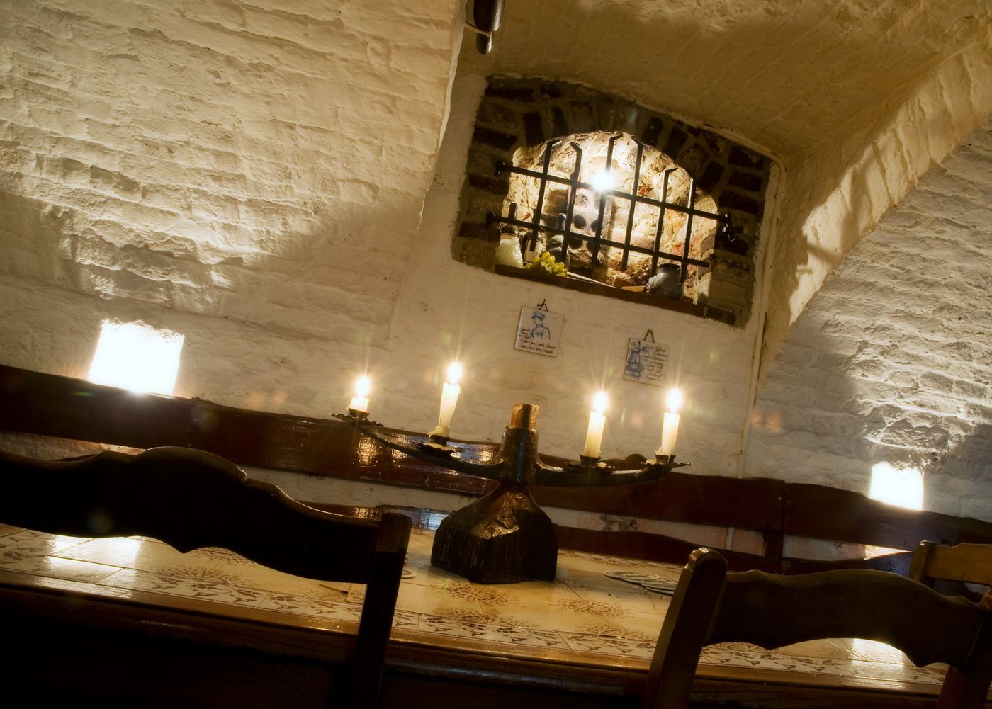 A dimly lit room with stone walls, a wooden bench, and a table with candles.