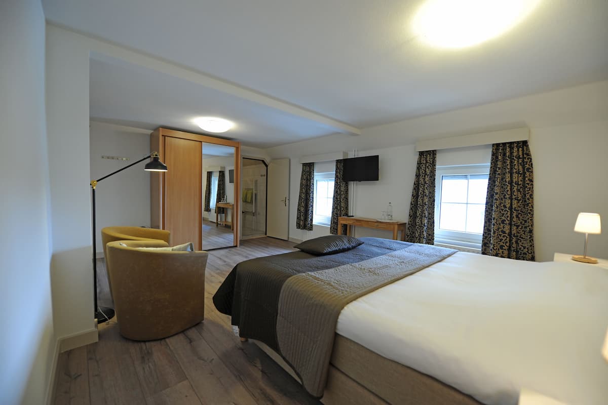 Hotelkamer met een groot bed, een stoel, een bureau, een televisie en een raam met gordijnen.