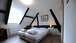 Une chambre à coucher avec un grand lit, deux tables de chevet, une commode, un radiateur, une fenêtre et un tableau au mur.