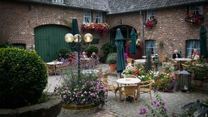 Une cour bordée de bâtiments en briques, avec des tables et des chaises à l’extérieur, ainsi que des plantes en pot.