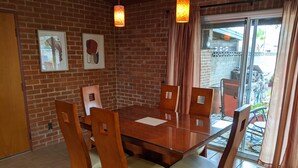 Een eetruimte met een glazen tafel en houten stoelen, een bakstenen muur en een glazen schuifdeur naar een terras.