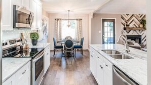 A modern kitchen with white cabinets, stainless steel appliances, and a dining area with a chandelier.