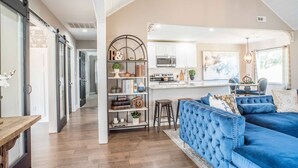 A spacious living area with a blue sofa, a bookshelf, and a kitchen area with white cabinets and a microwave.