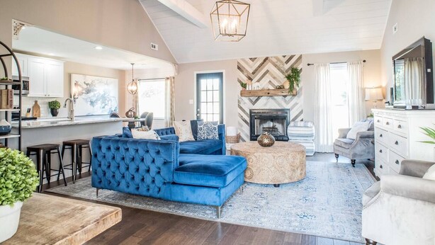 A spacious living area with a blue sofa, a fireplace, and a kitchen in the background.
