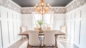 A dining room with a wooden table, four chairs, a chandelier, and patterned wallpaper.