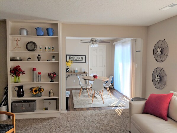 A living room with a sofa, a dining area with a table and chairs, and a kitchen area with shelves and appliances.