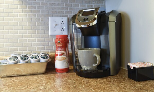 Una cafetera, una taza de café, una botella de leche para café y una bandeja con cápsulas de café sobre una encimera de cocina.