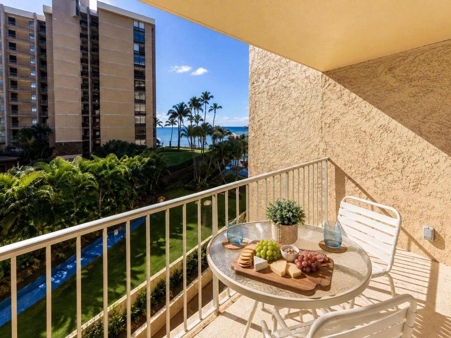 Un balcon avec une table dressée pour un repas, donnant sur une piscine et des palmiers.