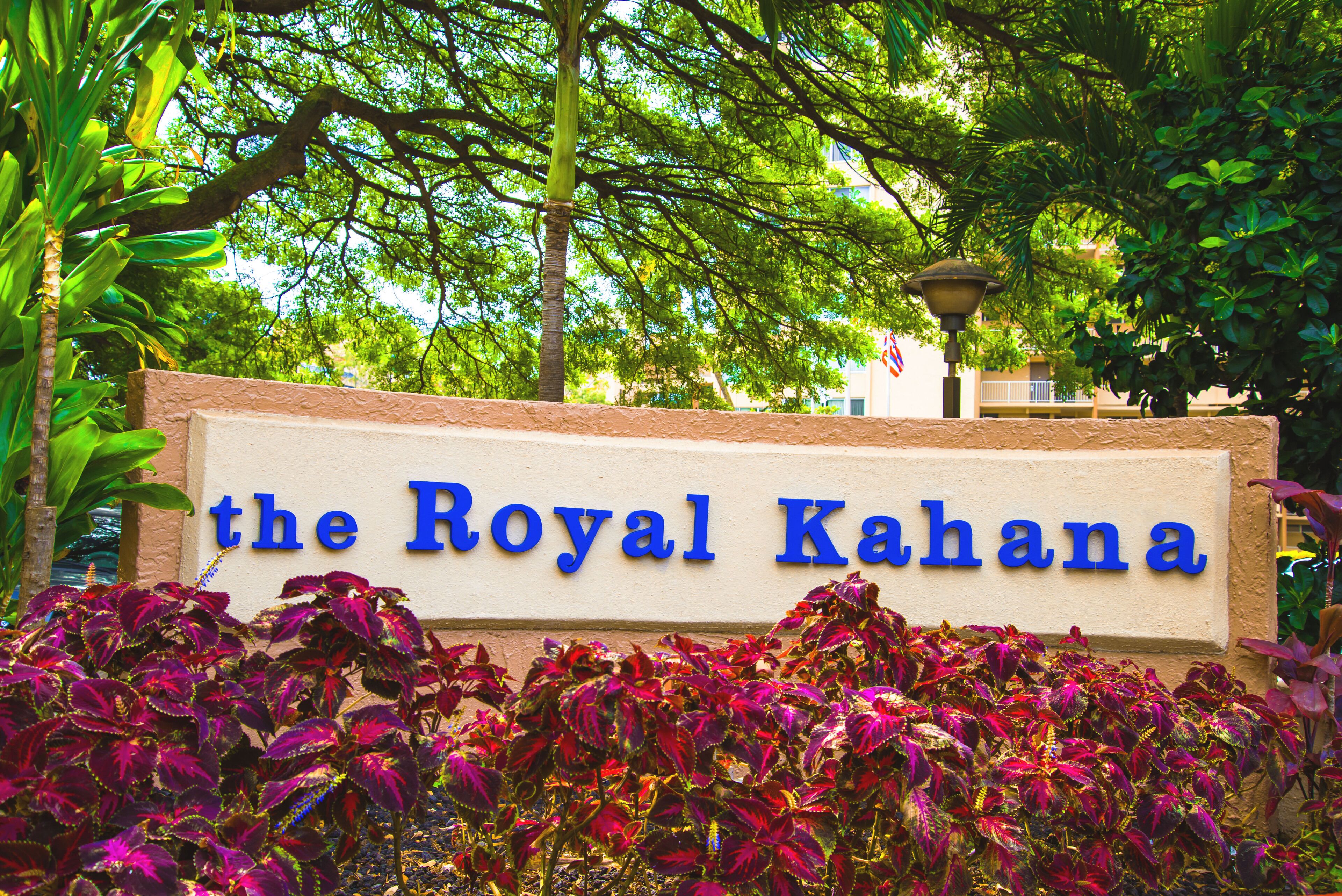 A sign reading "the Royal Kahana" with a backdrop of lush green trees and vibrant foliage.