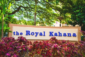 Un letrero que dice "the Royal Kahana" con un fondo de árboles verdes y follaje vibrante.