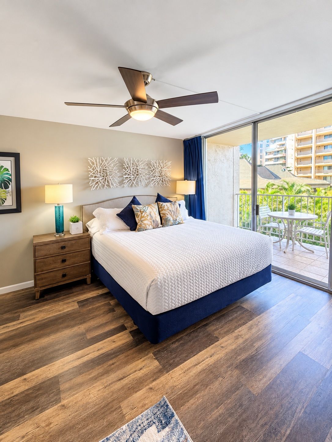 Un dormitorio con cama, mesita de noche, ventilador de techo y vistas al exterior.