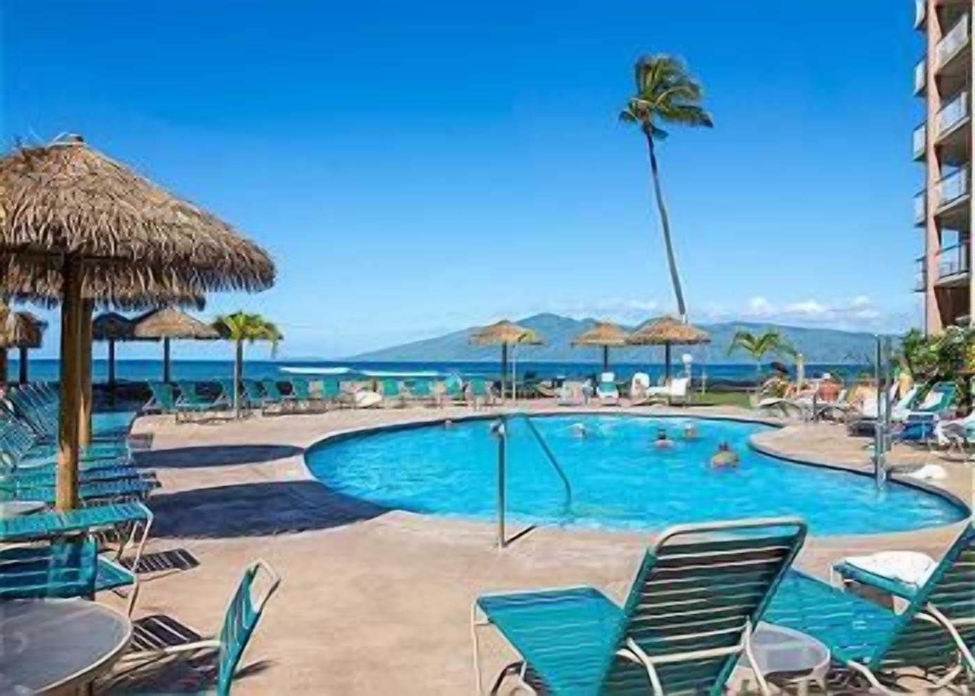 Un espace piscine avec des chaises longues et des parasols, un ciel dégagé et une vue sur l’océan.