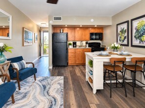 A modern kitchen with wooden cabinets, a black refrigerator, and a dining area with a white island and bar stools.