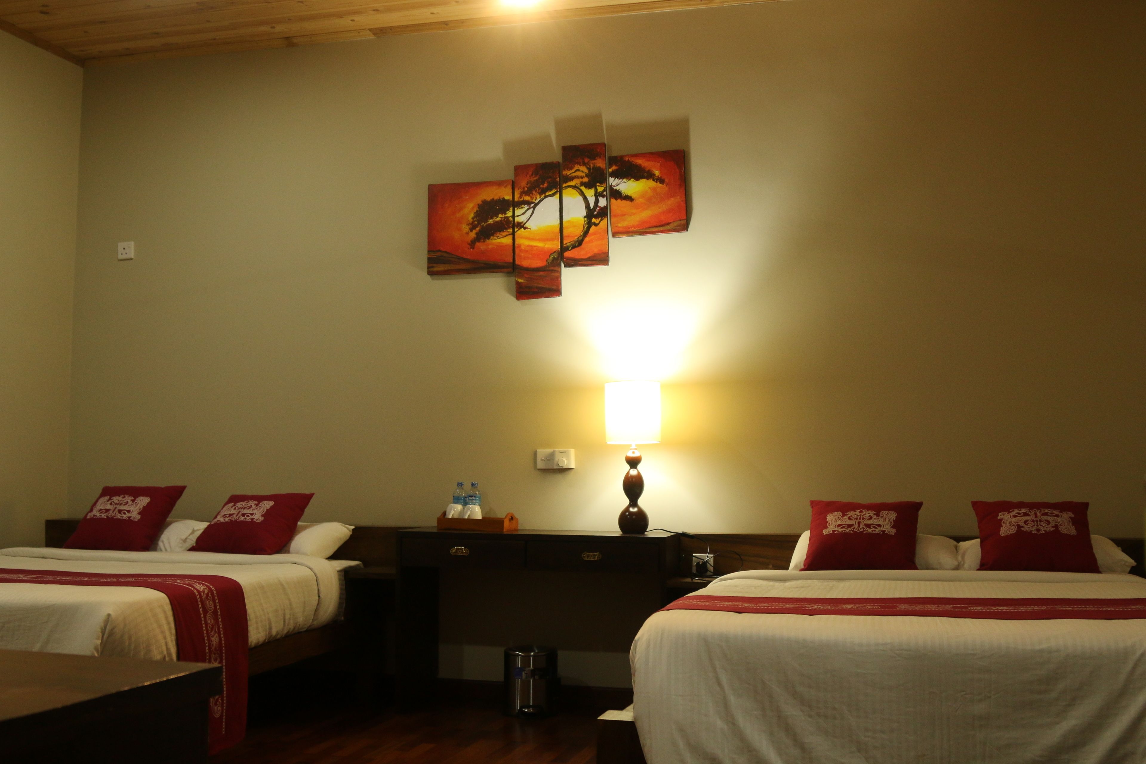 A hotel room with two beds, a nightstand, a lamp, and a wall-mounted painting.