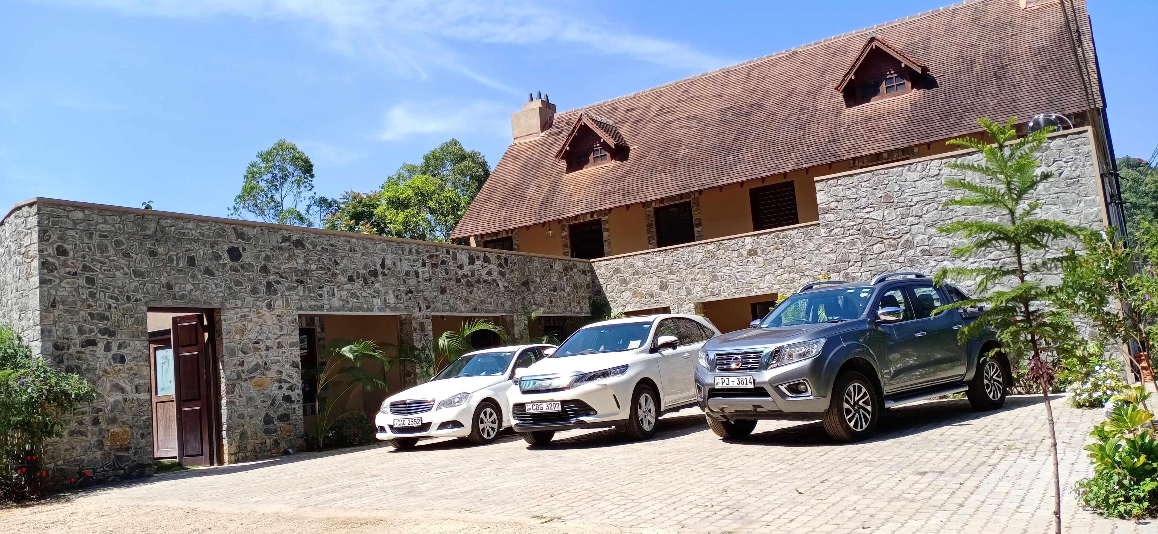 A stone building with a tiled roof, two parked cars, and a clear sky.