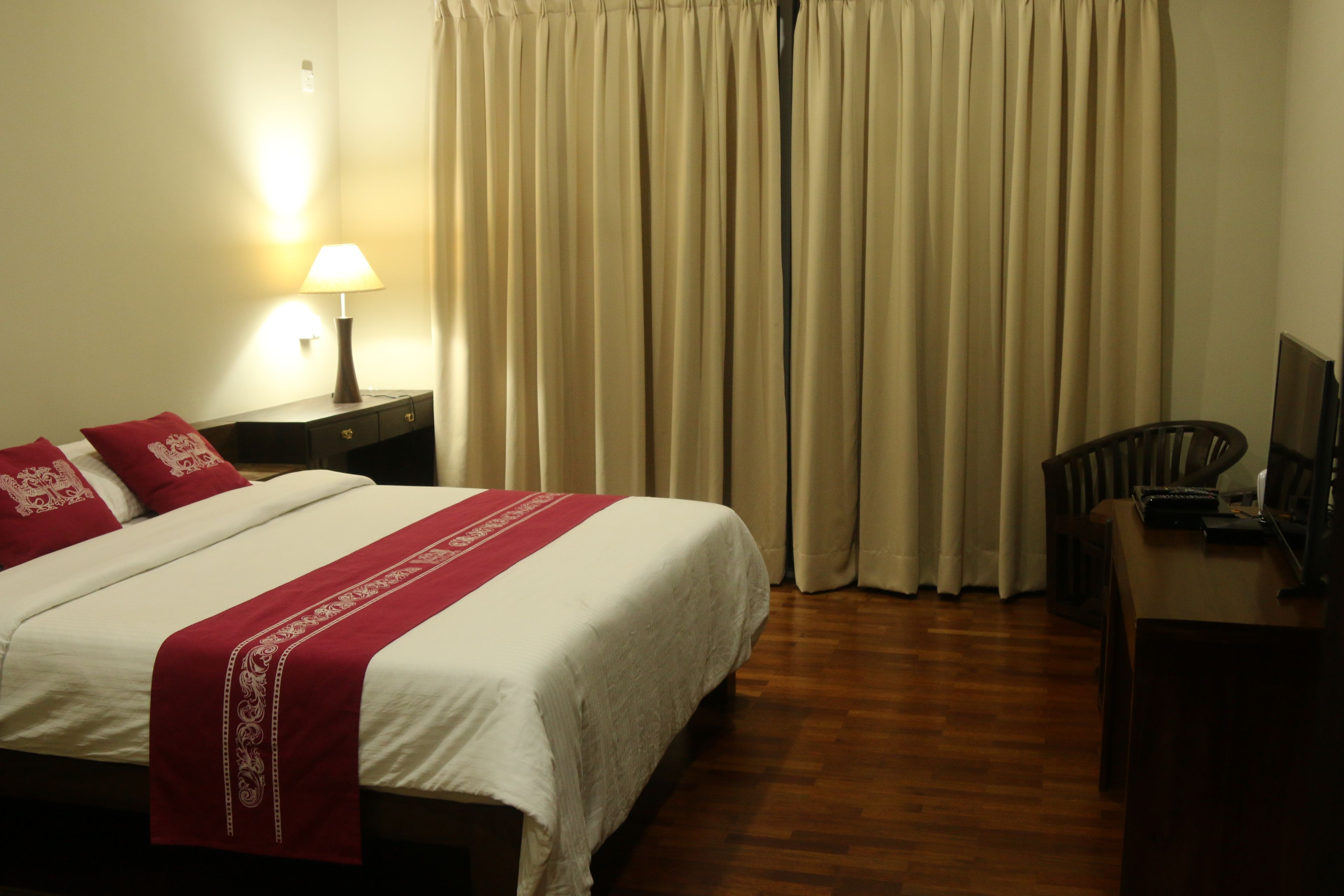 A hotel room with a bed, a desk, a lamp, and curtains.