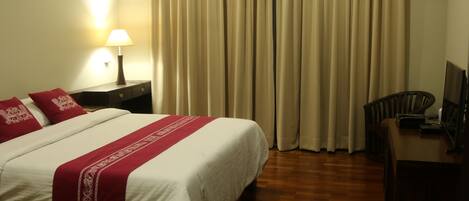 A hotel room with a bed, a desk, a lamp, and curtains.