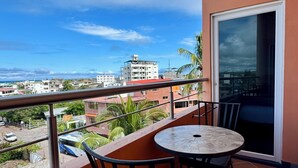 A balcony with a table and chairs, overlooking a cityscape with buildings and palm trees. - The Oceanview two-bedroom with balcony (Puerto Ayora, Santa Cruz Island)