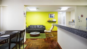 Un salon moderne comprenant un coin repas, un mur d’accent vert, un canapé en cuir noir, une table basse ronde et un comptoir de cuisine.