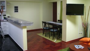 Un espace de vie compact comprenant un coin cuisine, une table à manger et un téléviseur fixé au mur.