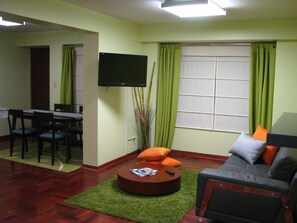 Een woonkamer met een bank, een salontafel, een flatscreen televisie en een eethoek met stoelen en een tafel.