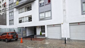 Un immeuble à plusieurs étages devant lequel est garé un SUV rouge, avec un petit cône orange et un panneau indiquant qu’il est interdit de se garer.