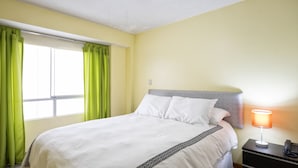 Un lit bien fait, avec du linge de lit blanc et un motif géométrique noir en bordure, une lampe de chevet et une table de chevet avec un téléphone.