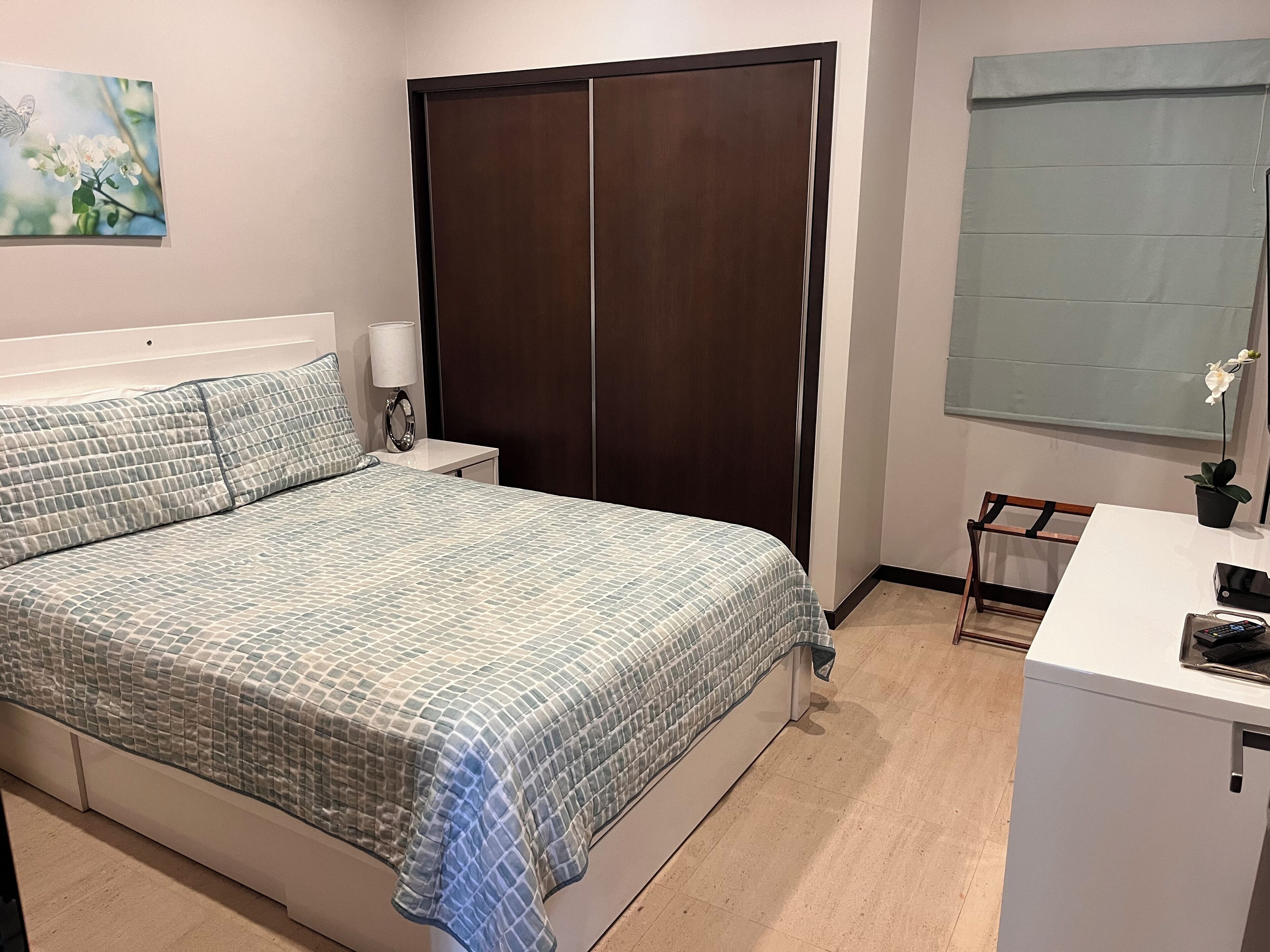 A bedroom with a bed, nightstand, dresser, and a window with a view of the outdoors.