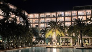 A hotel with a pool, palm trees, and a well-lit building facade.