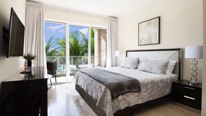 A hotel room with a large bed, a desk, a chair, a TV, a lamp, and a view of palm trees through the window.