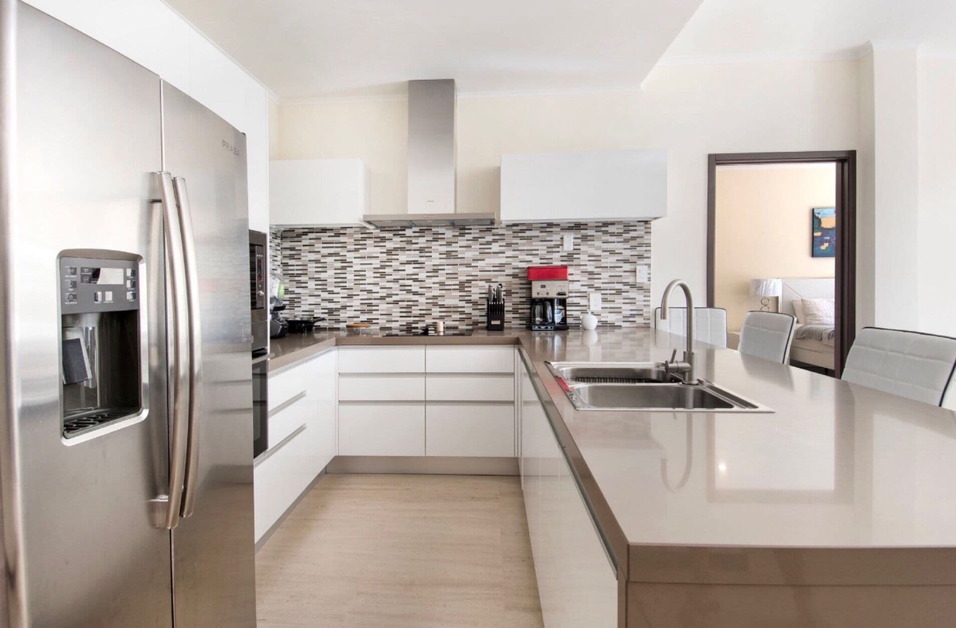 A modern kitchen with a stainless steel refrigerator, a built-in coffee maker, and a tiled backsplash.
