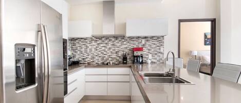 A modern kitchen with a stainless steel refrigerator, a built-in coffee maker, and a tiled backsplash.