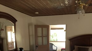 Un dormitorio con techo de madera, una cama con cabecera, un aparador, un espejo y una puerta que da a un balcón.