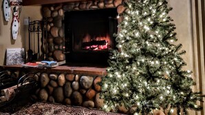 A cozy living room with a stone fireplace, a Christmas tree, and festive decorations. - Meadow Magic + FREE NIGHT! Spa, Gourmet Kitchen, 2 Free MTB's, 1hr2 Yellowstone (Big Sky)