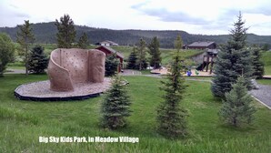 A playground with climbing structures and a slide, surrounded by trees and houses in Meadow Village. - Meadow Magic + FREE NIGHT! Spa, Gourmet Kitchen, 2 Free MTB's, 1hr2 Yellowstone (Big Sky)