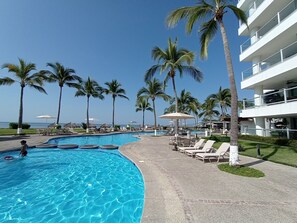 A resort pool with palm trees, lounge chairs, and a clear view of the ocean. - BEACH FRONT 3 BEDROOM CONDO NUEVO VALLARTA NEXT TO VIDANTA 4 GOLF COURSES NEARBY (NUEVO VALLARTA)