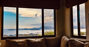 A room with a large window offering a view of a body of water and distant land.
