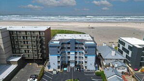 A multi-story hotel with a prominent entrance, parking lot, and a view of the beach. - OCEAN FRONT: SEASCAPE CONDO:  Seaside Vacation Homes, Inc Managed  (Seaside)